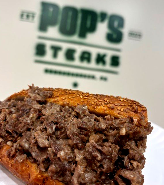 Cheesesteak In Front of Pop's Steaks Logo